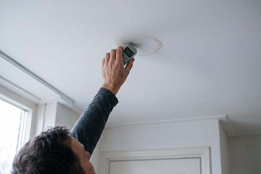 Specialist houdt een vochtmeter tegen een lichte vochtkring in een plafond