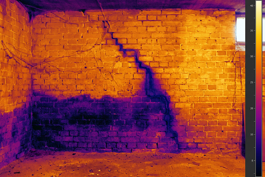 Warmtebeeld van een kelderwand, waarop zich onderaan een koudere natte band aftekent die langs een voeg omhoog loopt