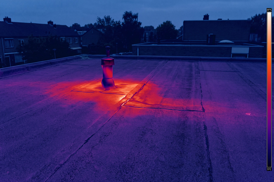 Warmtebeeld van een plat dak bij schemer, met een warme natte zone rond een dakdoorvoer